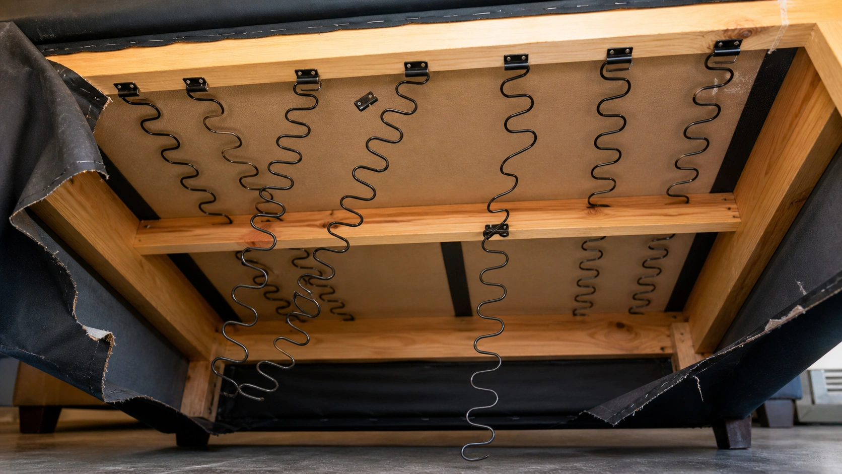 View underneath a sofa showing sagging and detached seat springs that need repair