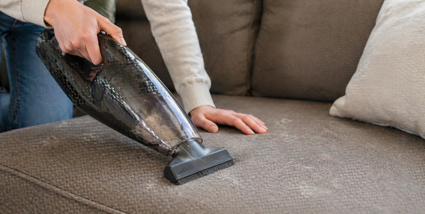 Person vacuuming pet hair from sofa using rubber brush attachment